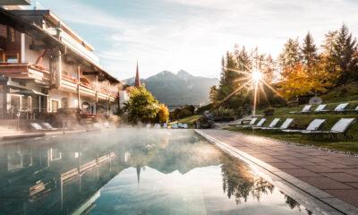 Der Außenpool im Herbst. Links ist noch das Hotel zu sehen, rechts stehen Liegestühle. Die Sonne strahlt tiefstehend durch die Bäume